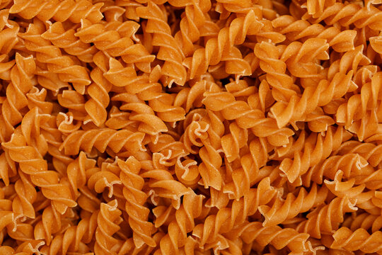 A detailed close-up view of uncooked whole wheat fusilli pasta forming a textured background.