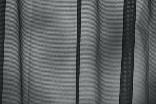 Abstract close-up of a black semi-transparent mesh fabric with vertical folds, ideal for dark textured backgrounds.