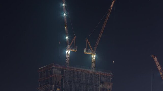 Tower crane floodlights overhead timelapse sequence captured clearly above Dubai. The towering crane structures are barely visible against the completely black night sky.