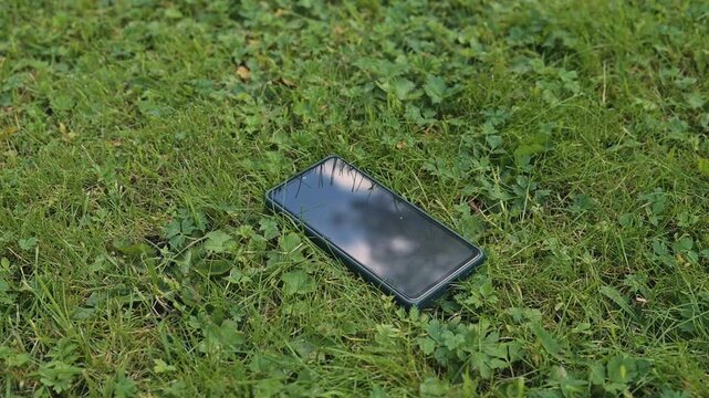 A smartphone is placed on the grass with the screen facing up, lose phone