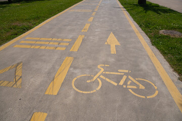 Obraz premium Concrete path featuring yellow painted road markings, including a bicycle symbol, directional arrow, and horizontal lines, defining a dedicated cycling lane