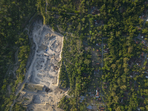 Aerial view of Sand and Stone Quarry showing excavated rocky terrain, heavy machinery, and surrounding lush tropical forest in Manisrenggo, Central Java, Indonesia.