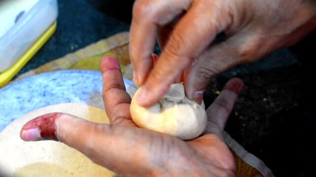 woman's hands stuffing a spiced lentil or dal filling into wheat dough balls in a home kitchen, preparing traditional Indian stuffed paratha or dal puri. 