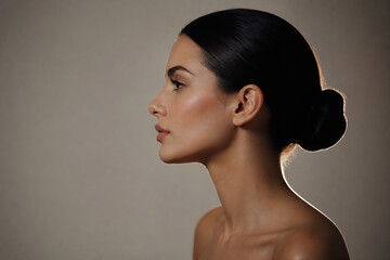 Obraz premium A woman with dark hair styled in a bun is shown in profile against a plain, neutral background.