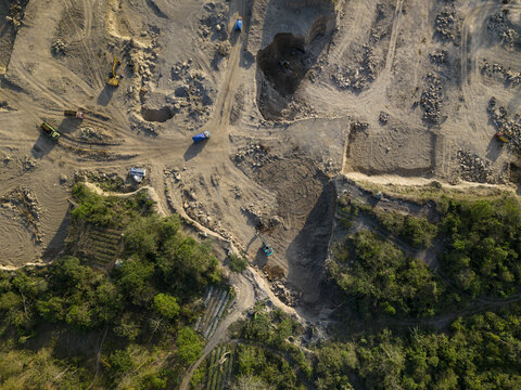 Aerial view of Sand and Stone Quarry with excavators and trucks on dusty ground surrounded by green trees in Manisrenggo, Central Java, Indonesia.