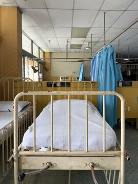 Interior view of an old public hospital ward showing vintage chipped metal medical beds with white sheets and blue privacy curtains