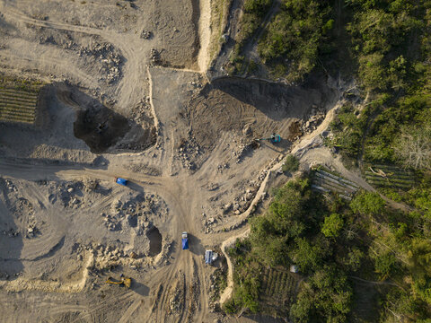 Aerial view of Sand and Stone Quarry with heavy machinery and trucks operating in a mining site near lush vegetation in Manisrenggo, Central Java, Indonesia.