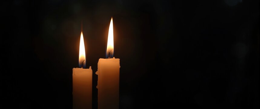 Two lit candles against a dark background