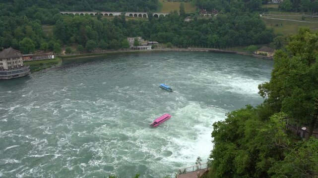 Rhine Falls Switzerland. Tourist boats floating in the turbulent river water near the forest bank and stone bridge. Water waves top view. Nature