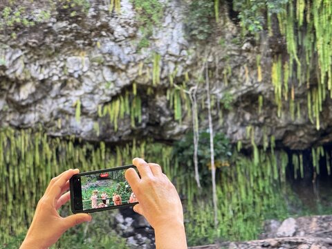 21 October 2024, USA, Hawaii, The Garden Isle, Kauaʻi, Kapaa, Wailua River, Fern Grotto, Pu'uhonua - man filming natives performance of songs and stories of ancient history