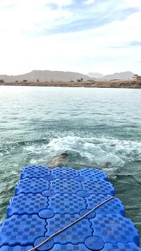 A teenage boy and his father perform somersaults, jumping with a running start off a swaying blue pontoon into the Red Sea in Sharm El Sheikh.