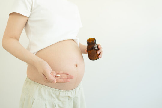 Pregnant woman holding dietary supplement pill and bottle against white background. Maternity prenatal care concept