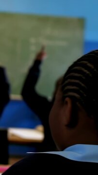 Vertical video: Watching boy in uniform in class, teacher asking at board, students raising hands