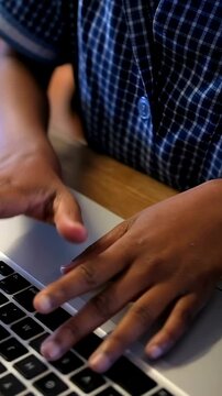 Vertical video: Placing palms child in blue checked shirt typing, working on silver laptop on table