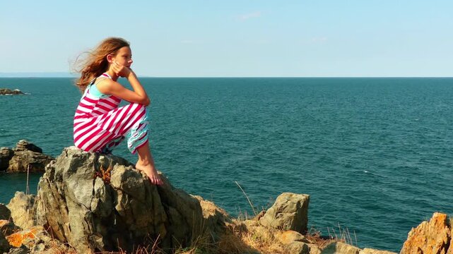 Little girl sitting on rocky shore of sea