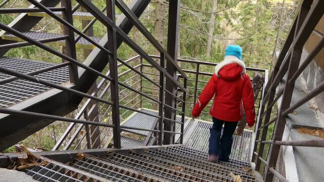 Beautiful girl in a red jacket is walking on a metal staircase.
