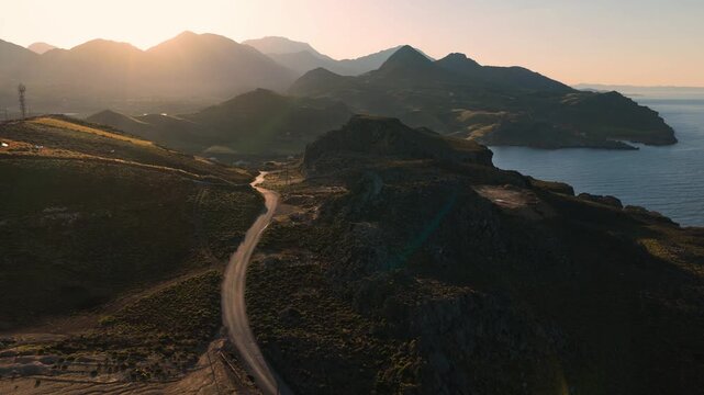 Sunrise scenery on Crete Island coastline with winding road through the high mountains, drone aerial view
