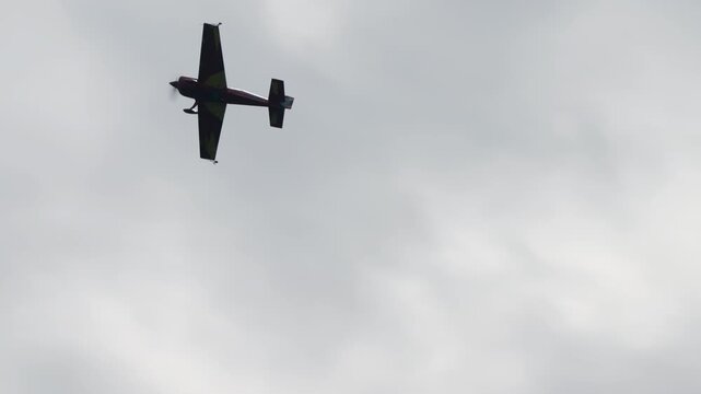 Stunt plane descending in a steep dive, aerobatic aircraft dropping nose down against a cloudy grey sky, single engine sport plane at an air show, captured in slow motion