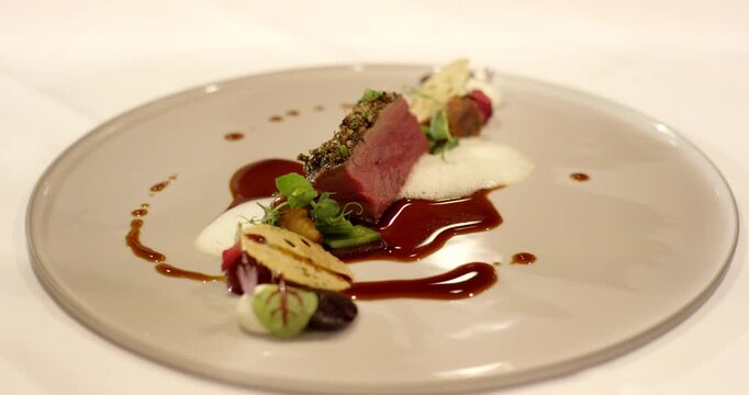 Elegant fine dining main course served on a beige plate featuring meat white foam and a rich dark red sauce