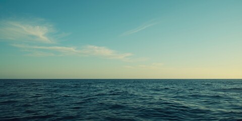 Fototapeta premium Tranquil ocean scene featuring a clear blue sky and soft wispy clouds on the horizon