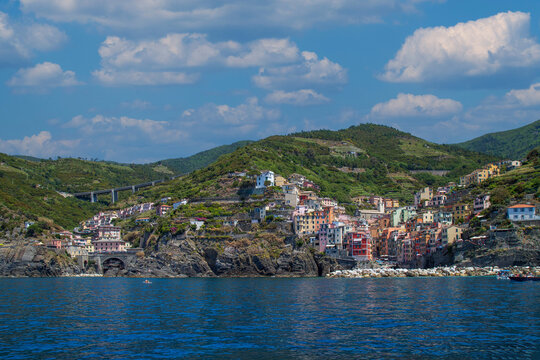View from the sea of ​​Riomaggiore, one of the  Cinque Terre villages, a steep cascade of pastel houses descending towards a small harbor carved between dark cliffs. Liguria, La Spezia, Italy.