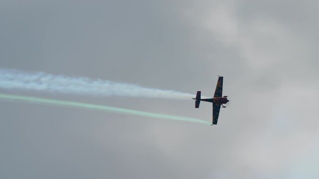 Stunt plane banking hard, aerobatic aircraft trailing green and white smoke across a grey sky, single engine sport plane carving a turn at an air show, captured in slow motion