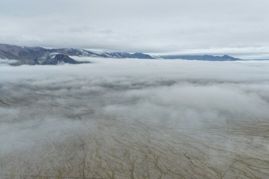 Aerial view of Kviarjokull glacier landscape with low clouds covering the vast outwash plain and distant mountains under an overcast sky, Hofn, Sveitarfelagid Hornafjordur, Iceland.