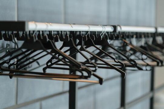 Close view of empty black hangers lined on rack inside clean retail interior with soft light by dawn rack