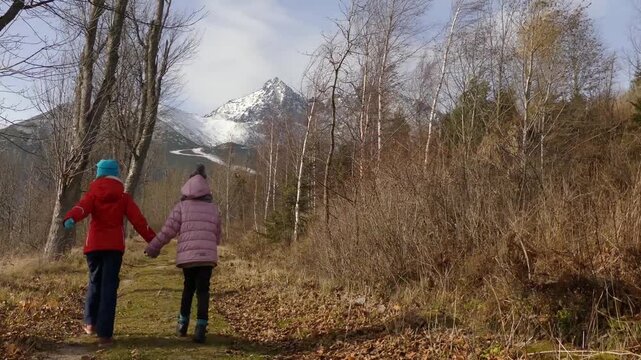 Two little sisters walk during a strong wind in the autumn forest, background is Lomnicky stit, High Tatras, Slovakia.