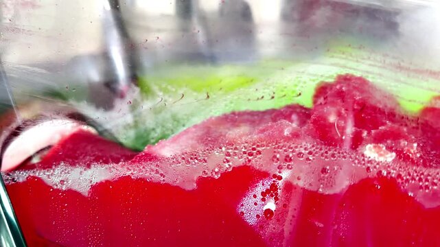 Closeup of a commercial icy drink machine, with an auger mechanism churning pink red slush, ready to deliver on demand a semi frozen, sweet beverage.