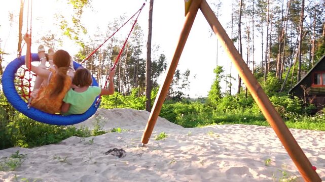 Two sisters ride a round swing in a city resort park. White shallow sand.