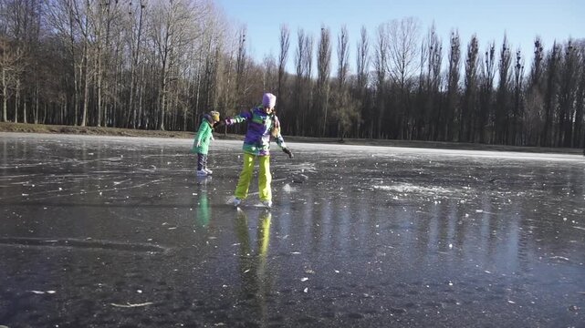 Slow motion. Two girls sisters skate on ice frozen lake. Winter city park.