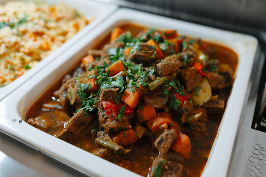 Slow cooked beef stew with carrots, peppers, potatoes and herbs in serving tray beside light rice ready