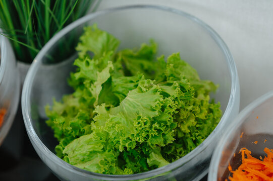 Bright lettuce fills clear bowl with shredded carrot and herbs suggesting fresh salad prep indoors daily