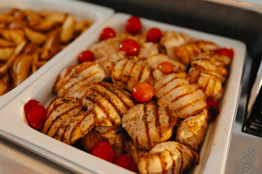 View of grilled chicken slices in serving tray with cherry tomatoes beside dishes at buffet display areas