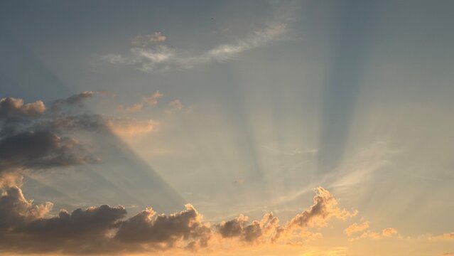 Crepuscular rays breaking through dark clouds in evening sky. Beautiful scenic view of sunbeams and dramatic light breaking through soft clouds during golden hour sunset in blue sky