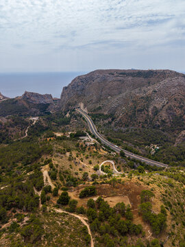 Aerial view of a winding highway passing through a mountain tunnel near the Mediterranean coast with rugged hills and sparse vegetation in Calp, Valencian Community, Spain.