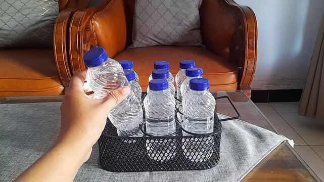 Took and placed a bottle of mineral water on the black metal bottle rack. The mineral water was in the living room on a wooden table with a gray tablecloth.
