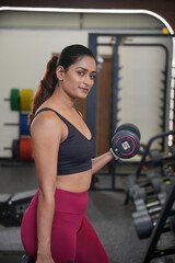 Fototapeta premium Maharashtra, Sion, India- 22nd March 2026- Young Indian girl in her active wear doing workout with dumbbells in gym. 