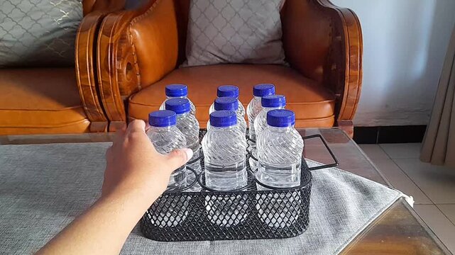 Took and placed a bottle of mineral water on the black metal bottle rack. The mineral water was in the living room on a wooden table with a gray tablecloth.