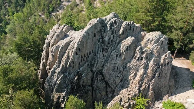 Thracian cult rock niches ancient sanctuary aerial view Bulgaria mysterious stone chambers mountain pine forest drone shot archaeology history discovery textbook illustration textbook media resource