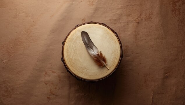 Top perspective of a meditation drum made from leather with sacred feather and sage smudge sticks on a smooth textured backdrop with copy space
