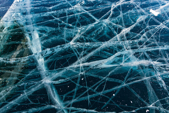 View of intricate patterns of deep cracks in the thick transparent ice of Lake Baikal, showcasing the natural beauty of the frozen surface in Khuzhir, Irkutsk Oblast, Russia.