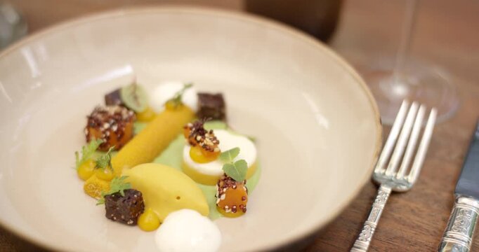 Gourmet dessert composition with mango sorbet cake bites and microgreens in a beige ceramic bowl