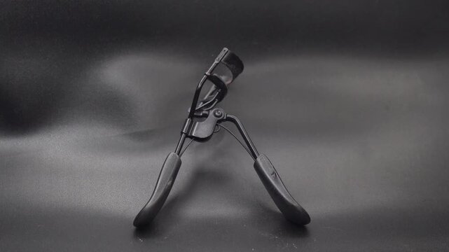 An old metal eyelash curler on a dark studio background.