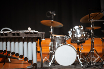 Obraz premium Selective focus on a metallophone percussion instrument at stage edge with blurred drum kit, cymbals and black backdrop prepared for a live concert