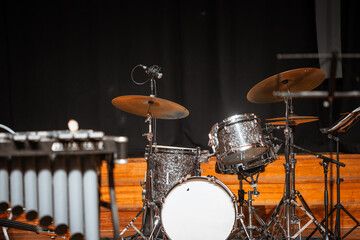 Obraz premium Selective focus on a polished drum set with cymbals and microphones on a wooden concert stage, ready for musicians before a live performance