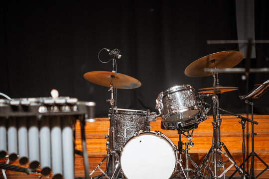 Selective focus on a polished drum set with cymbals and microphones on a wooden concert stage, ready for musicians before a live performance