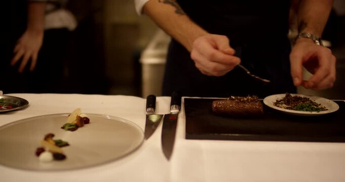Chef uses a spoon to carefully add finely chopped herbs and seasoning onto a piece of cooked meat