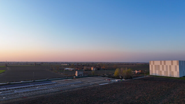 Expansive view of rural Italian landscape at dusk, featuring agricultural fields, buildings, and a large solar energy installation site under construction